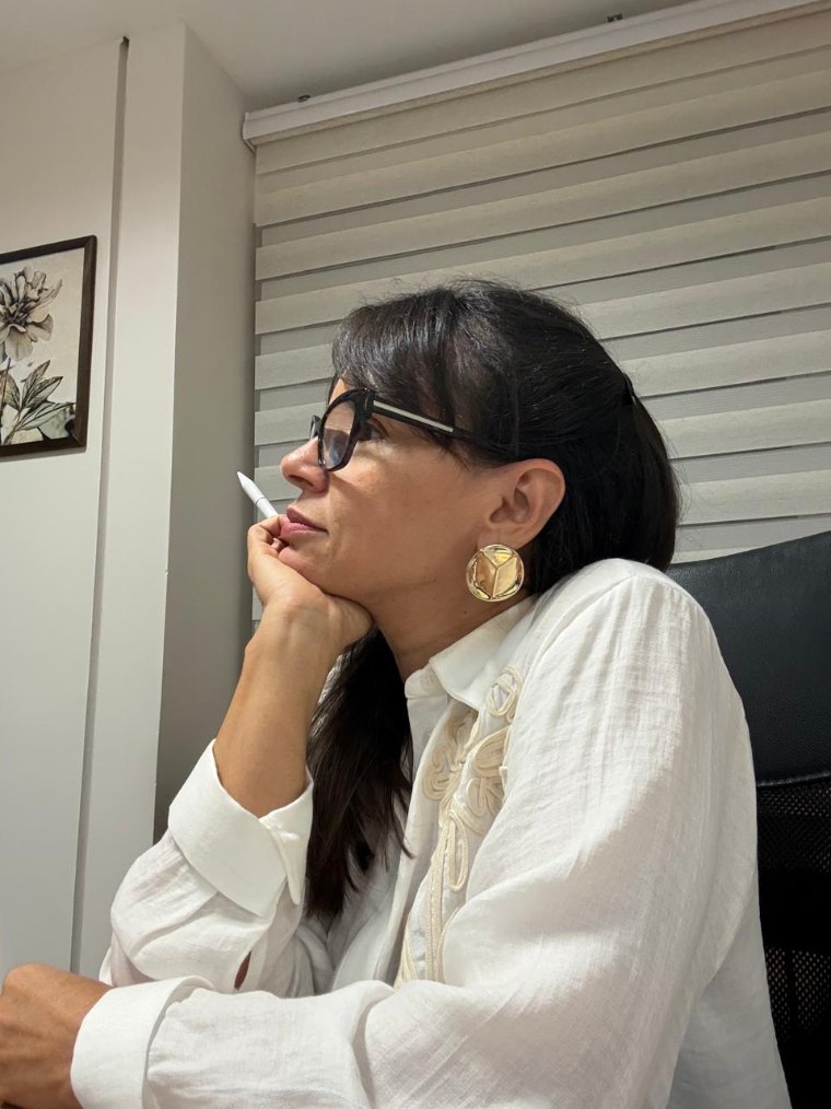Valquiria de perfil no consultório, apoiada na mão, em atitude de escuta atenta.